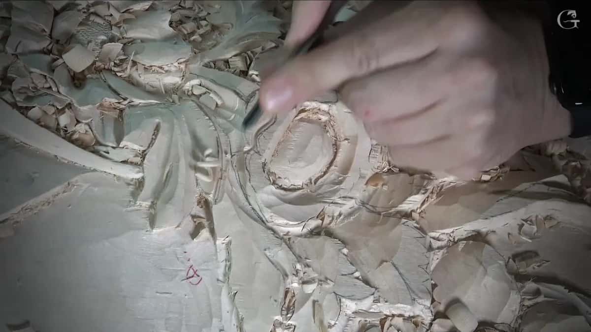 Fingers guide a narrow tool along the far side of the round flower
