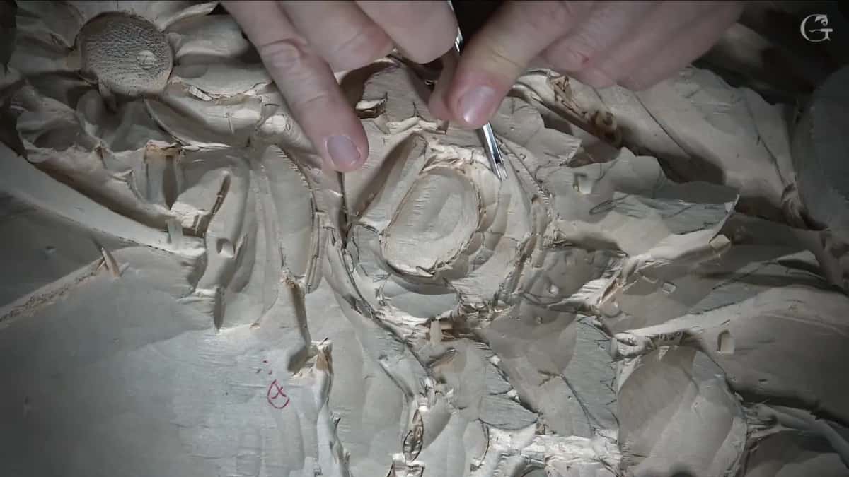 Two fingers pinch a slim tool near the flower's middle, the textured disc above