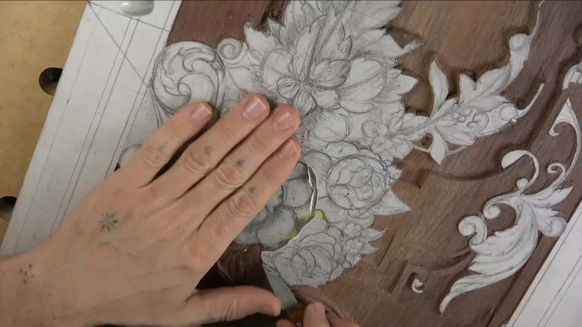 Flat hand holding the paper down while a blade works at the bottom edge of the frame