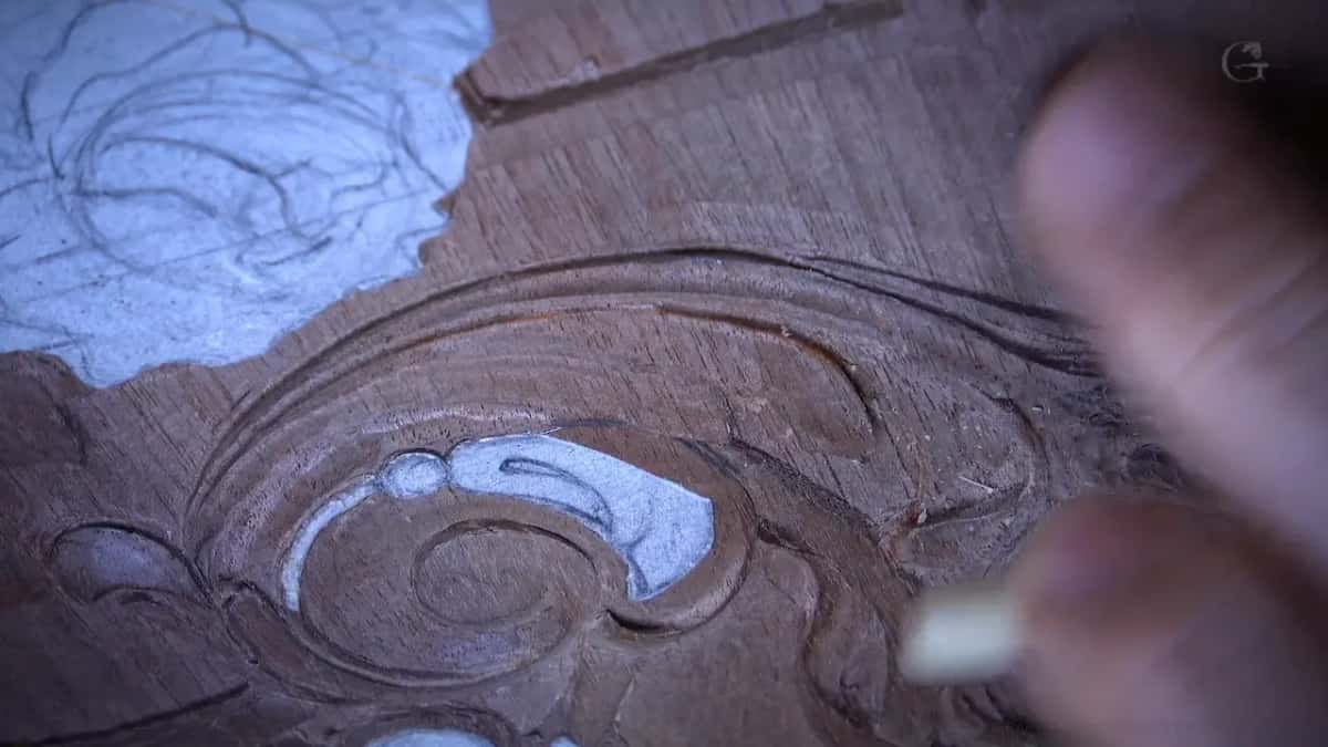 Blurred fingers at the right, a pale reed tube reaching in toward the finished scroll on the left