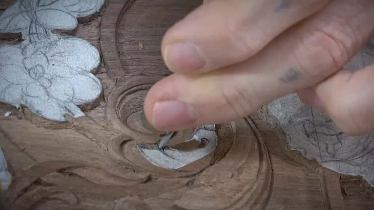 Fingertips resting over the carved spiral, nails catching the light, the shape half cut beneath them