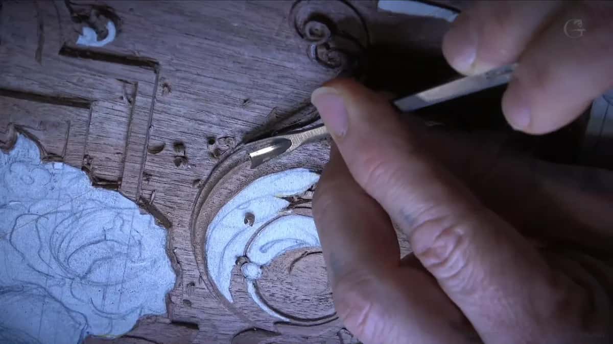 Two hands, one steadying and one holding a slim blade, working at the middle of the carved corner
