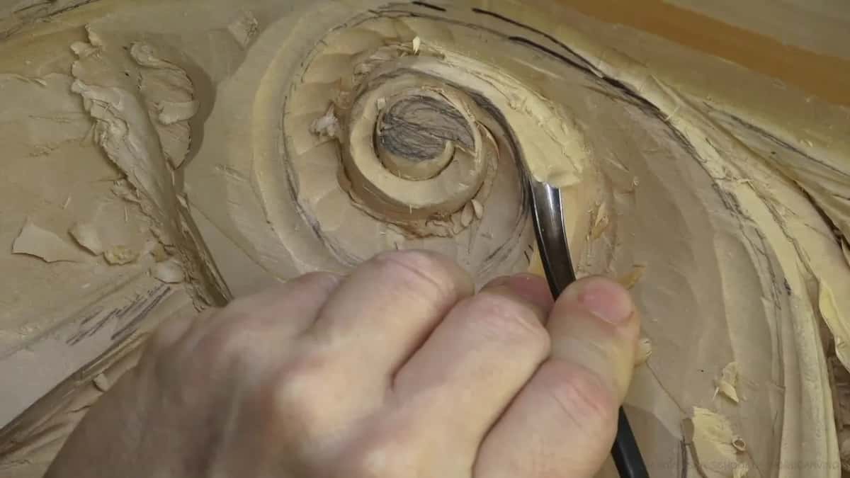 A hand steers a steel shank into the curved channel beside the spiral, shavings on the left.