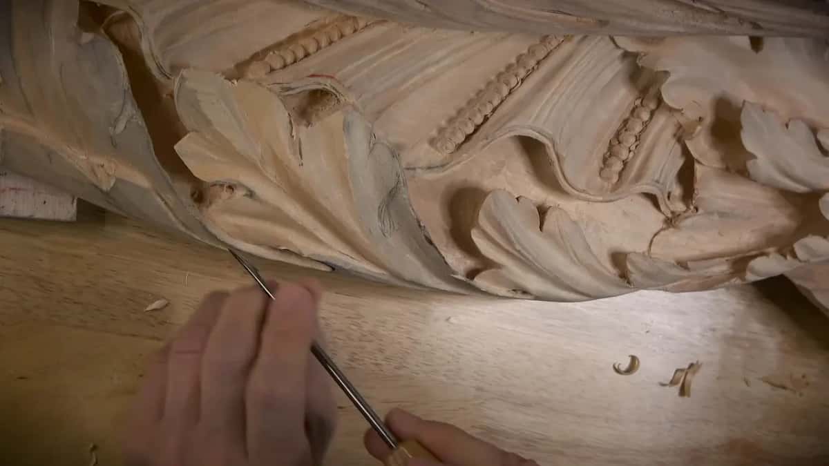 The pipe held Two hands guiding a long thin blade along the bottom edge of a frieze that carries a bead molding