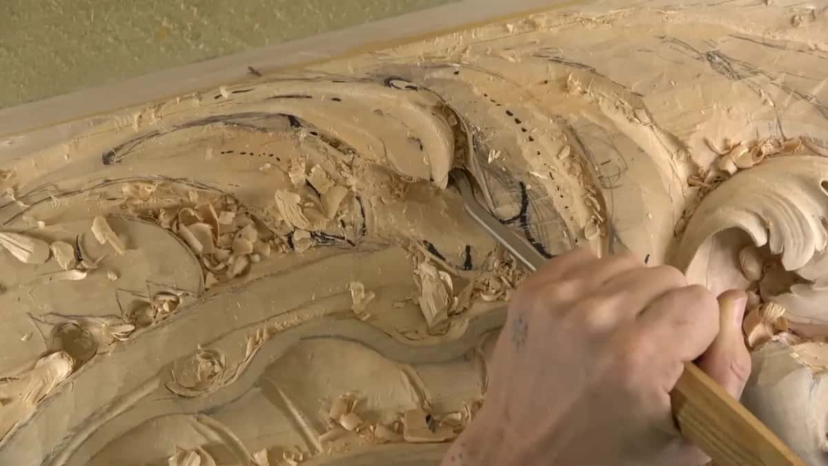 One hand works a gouge along the lobe while dark marker lines curve across the top.