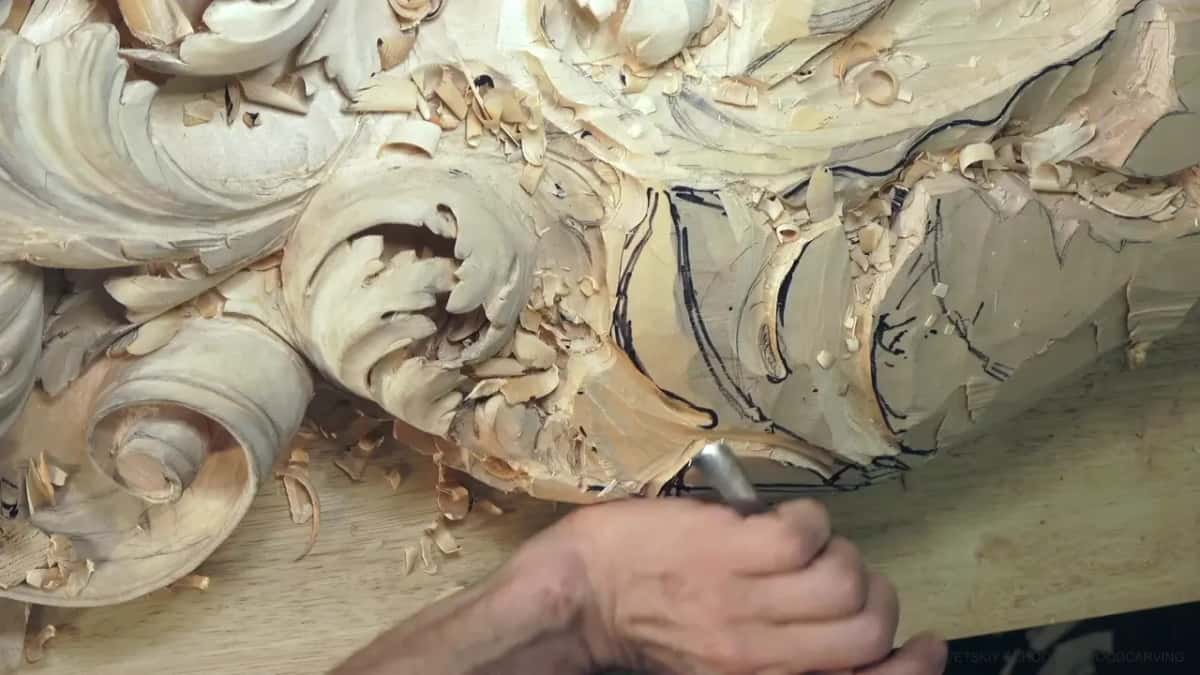 A gouge bites into the faceted block just below the finished scrolls.