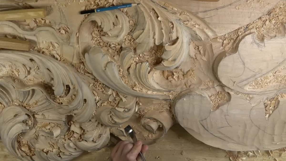 Down near the bottom edge, one hand works a small gouge beside the curl while the rest of the board waits.