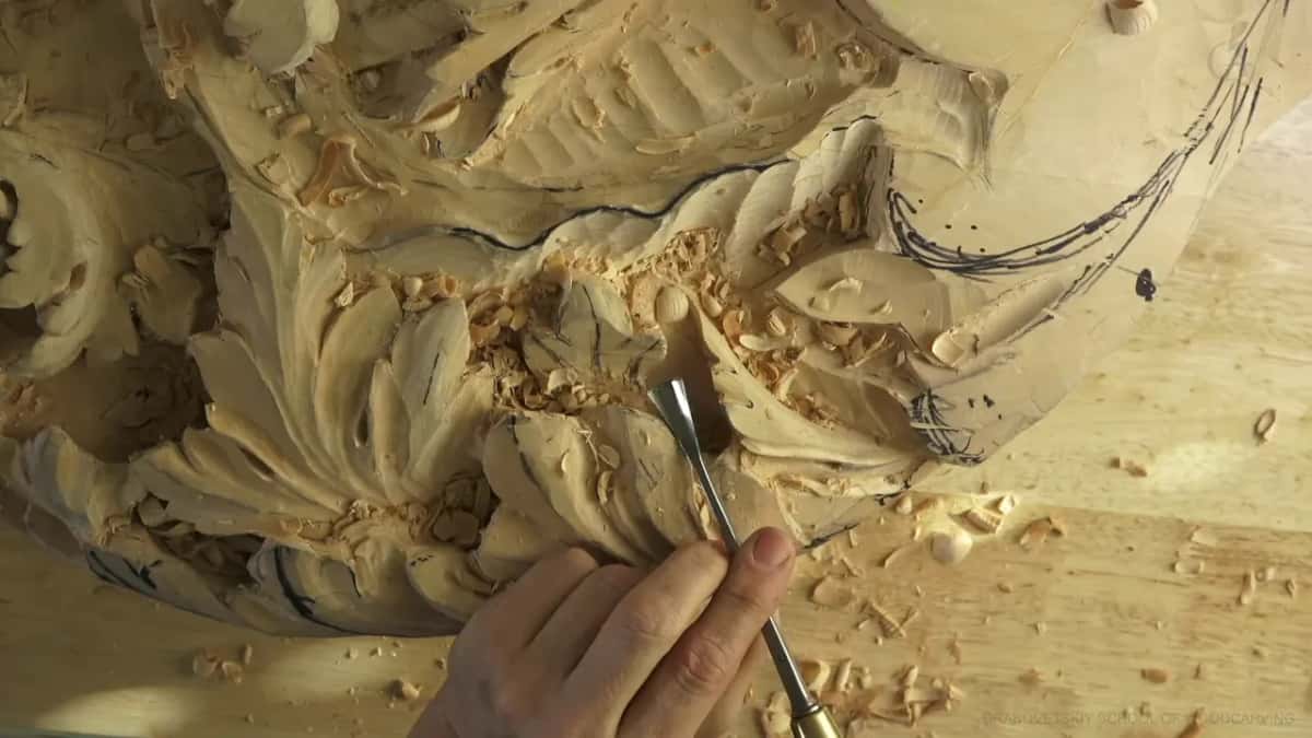 Deep in a concave full of chips, a gouge sits with carved leaves above and below it.