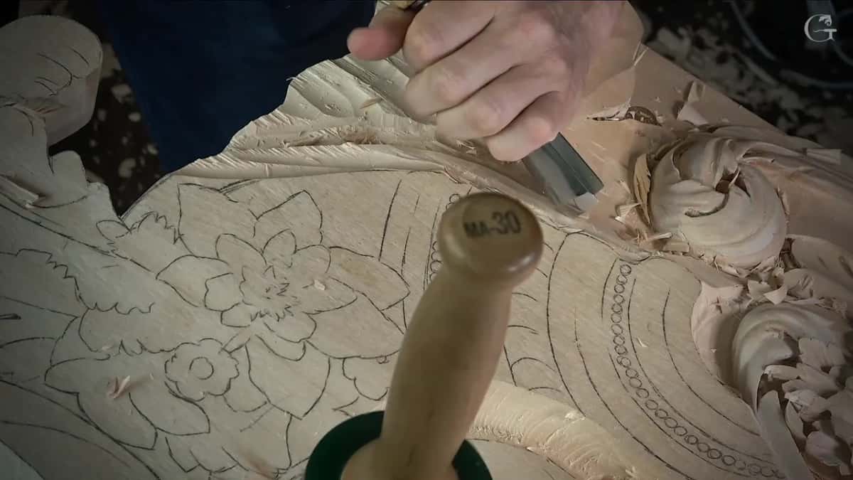 Hand on a gouge above the scroll, a mallet handle standing up in front