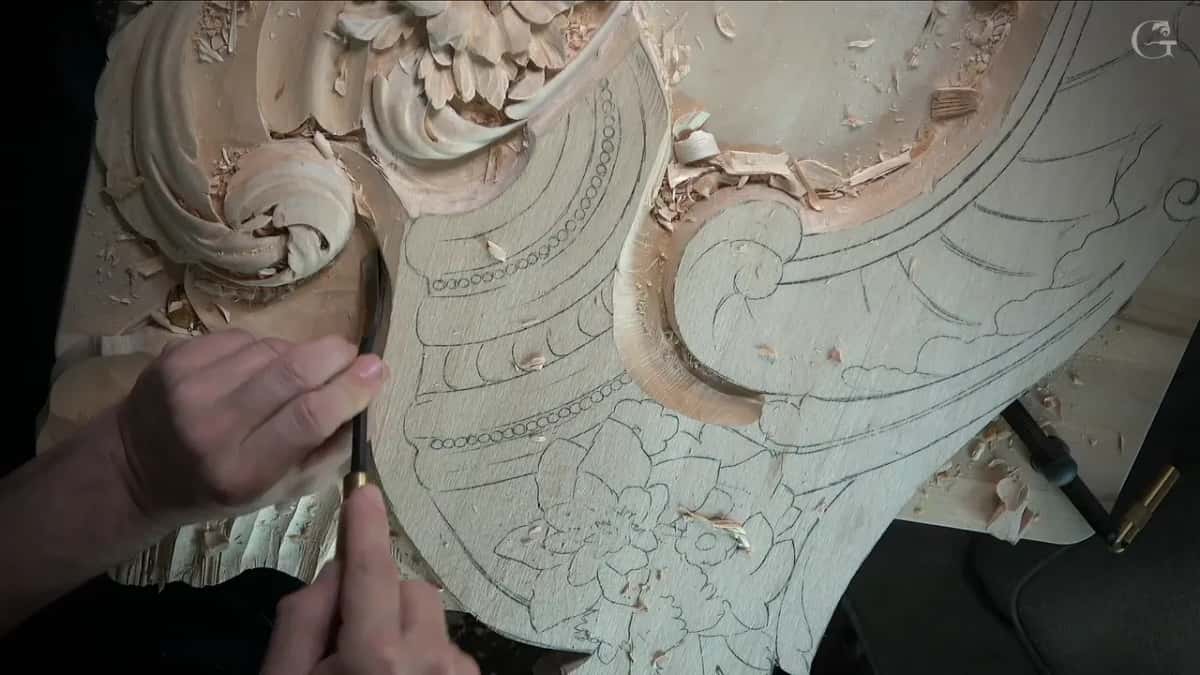 Two hands pinch a small tool against the inner corner of the scroll, lines drawn all around