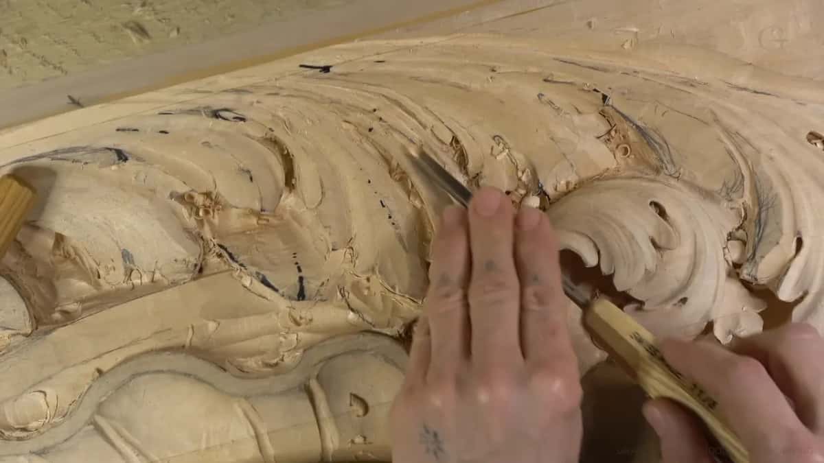 Hands steer a light handled gouge under the edge of a curl.