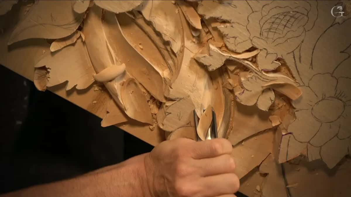 A narrow gouge stands almost upright in the hollow, the hand holding it low near the steel
