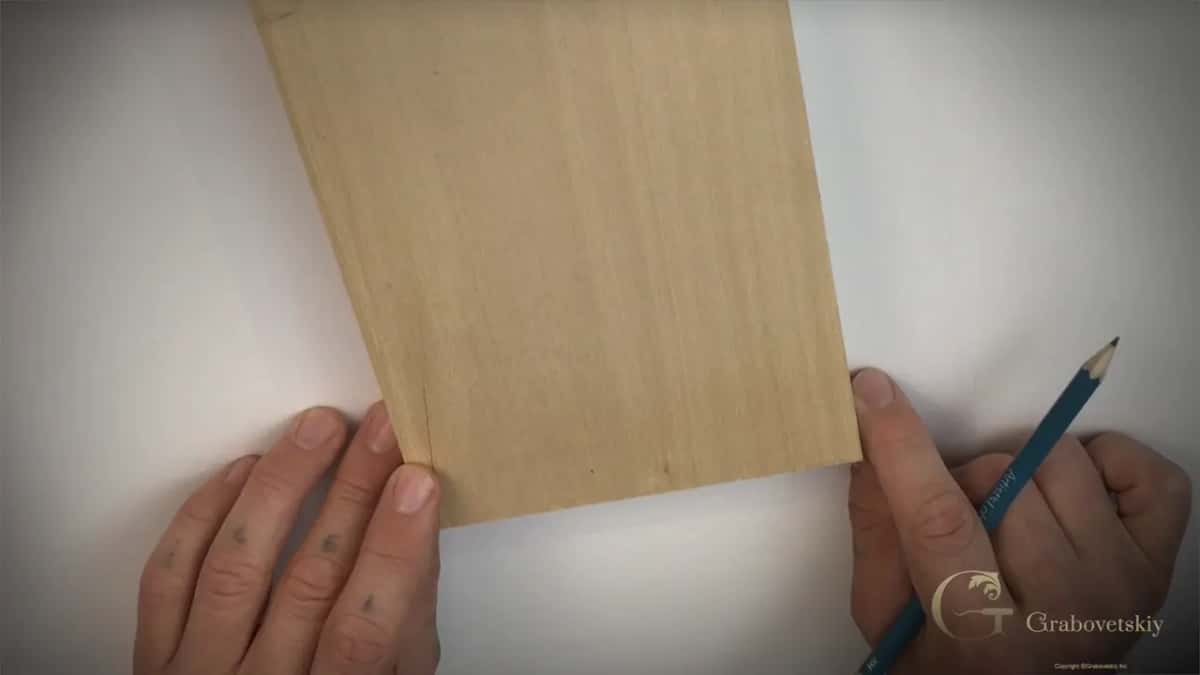 Block of pale wood held down on the sheet while a pencil runs round its edge