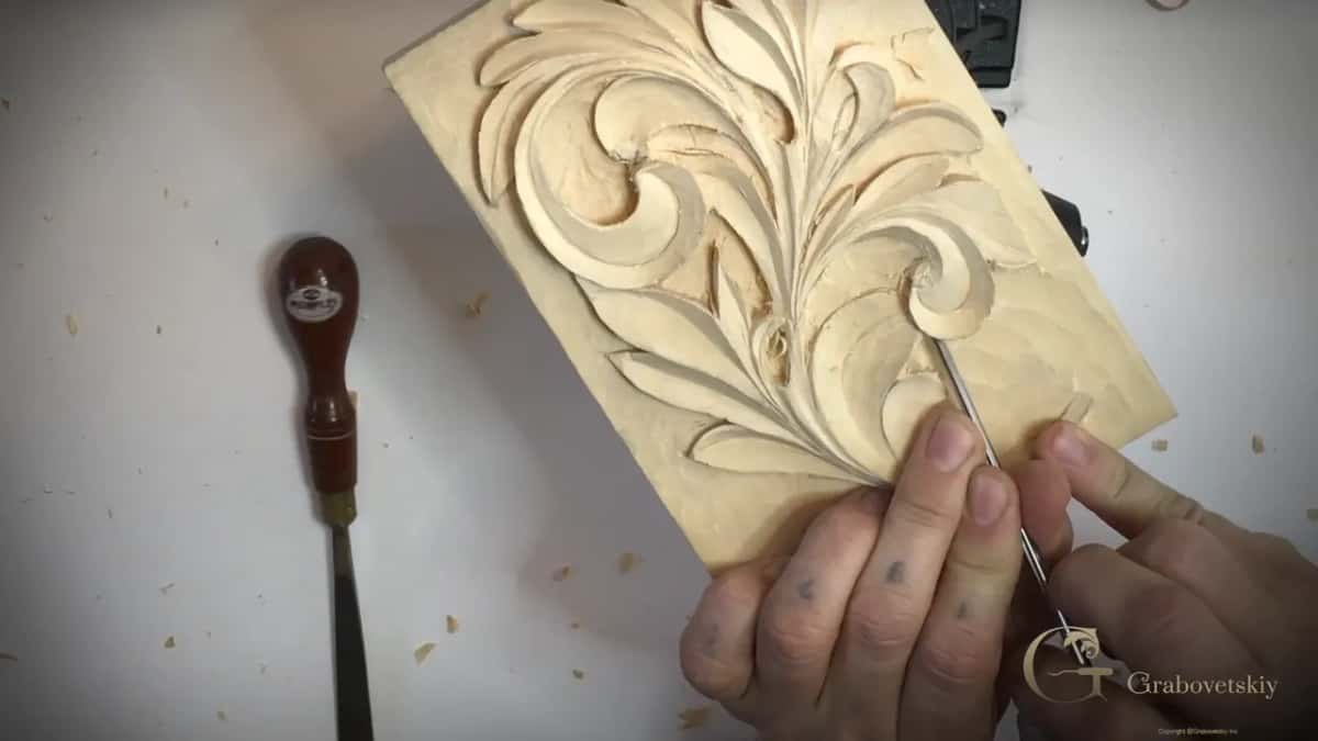 Red handled tool lying on the table while two hands work at the right curl