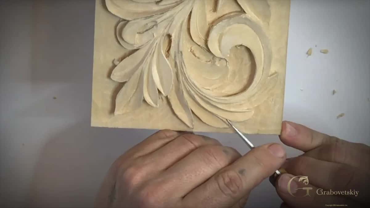 Thin pointed blade low at the right edge of the panel, both hands steadying it from below