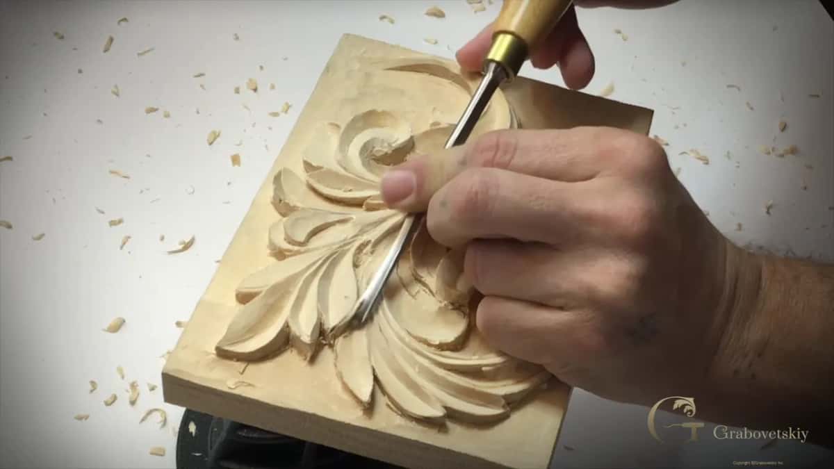 Straight gouge with a brass ferrule held low against a curl, fingers on the steel