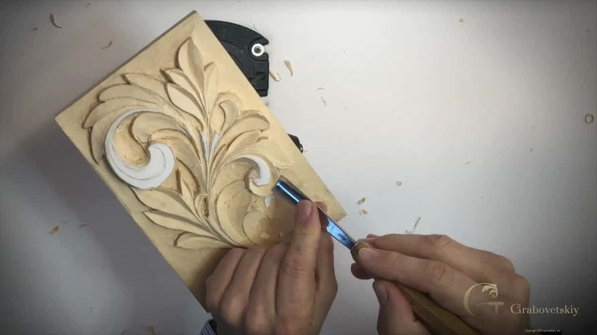Dark steel gouge held in both hands on the right side of the leaf, chips around the panel