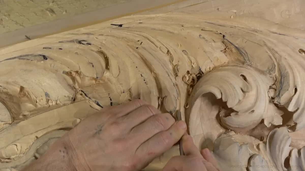 One hand lies flat on the board while the other holds a narrow tool straight up beside the curl.