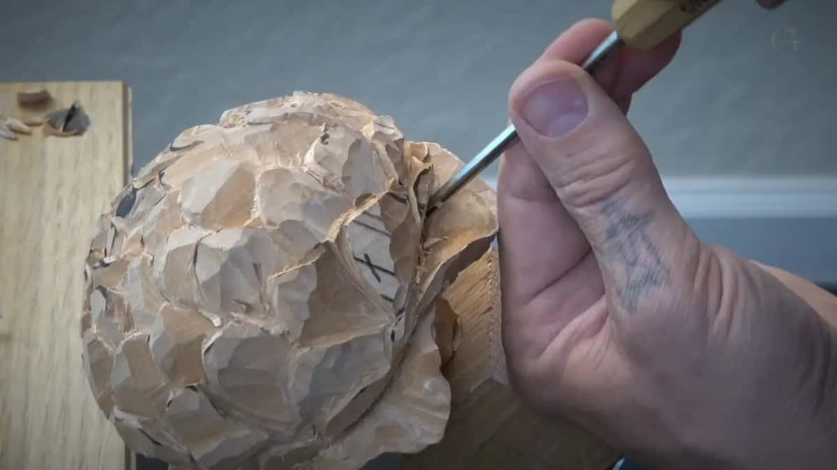 Peony on its block, a fine tool coming in from the right, held between two fingers rather than gripped.
