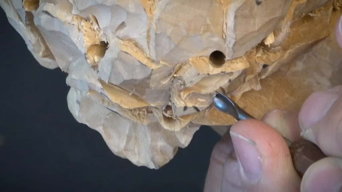 Three bored openings sit dark in the carved surface while a small gouge works at the lower right of the flower.