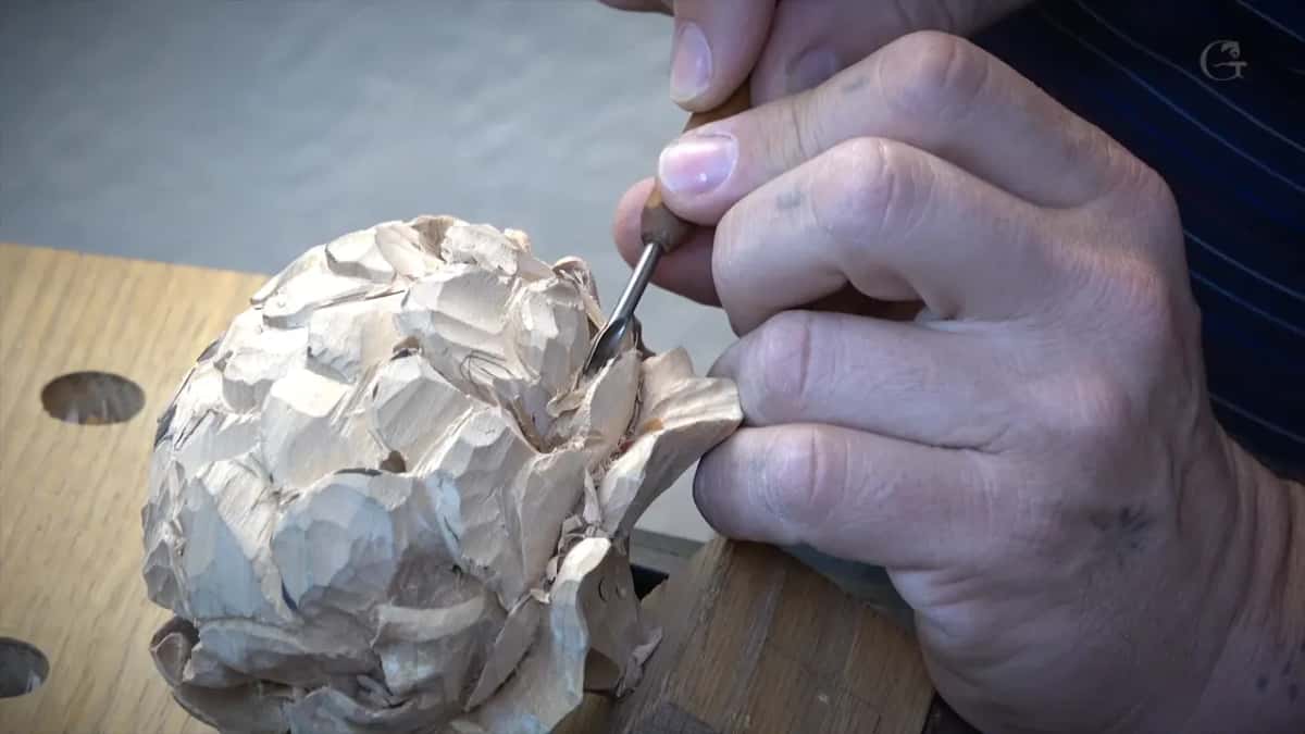 Both hands on the flower over the bench, a needle-fine tool somewhere in among the petals.