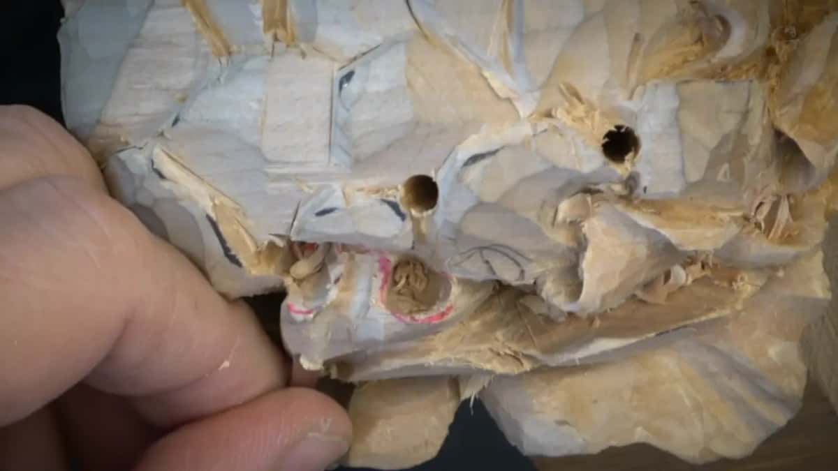 Fingers across the carved surface, openings and pink marker visible, a small tool arriving from the side.