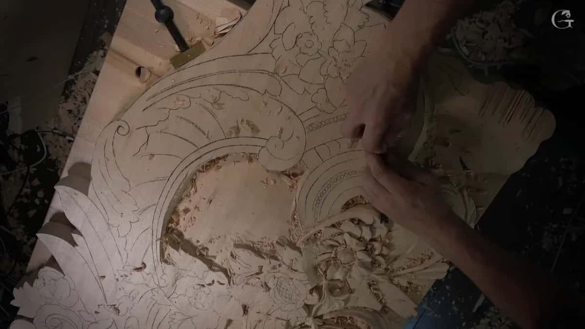 Board from above, one half carved and the other half still a pencil drawing, hands at work in the middle