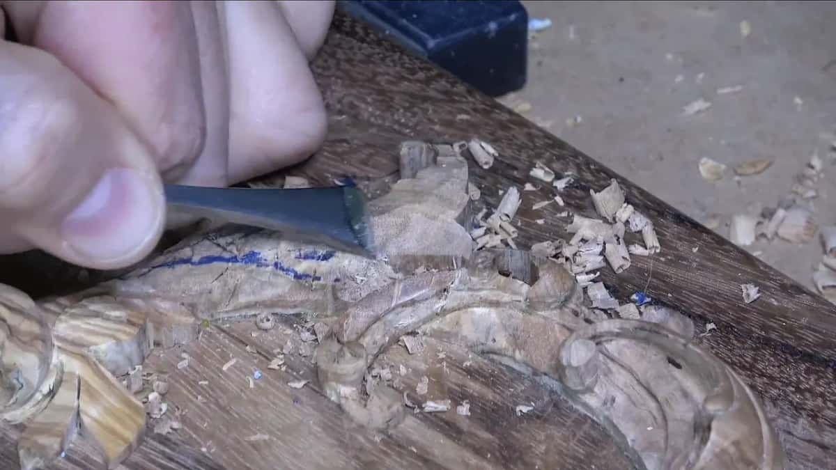 Close view of a wide, nearly flat gouge taking the high section down, with curled shavings piled beside the blue lines