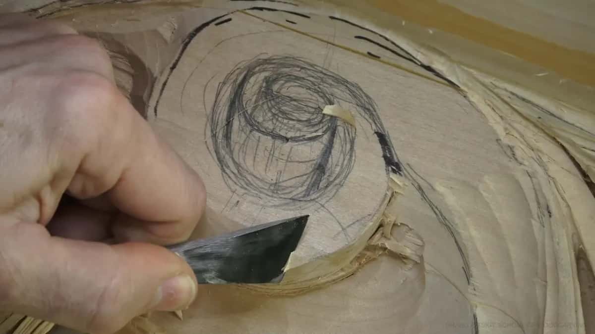 A flat blade slices the rim of a round top covered in pencil scribble.