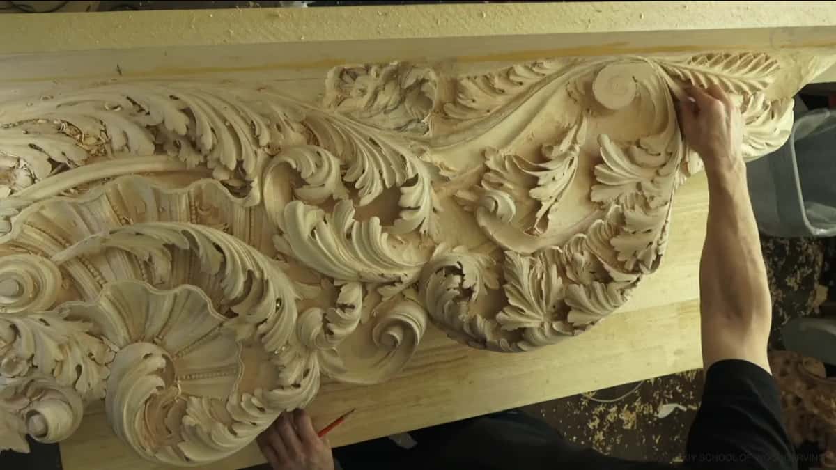 The whole carved board from above, one bare arm reaching up to a flat round disc near the top right.