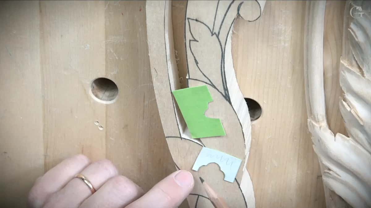 A scrap of green tape stiffening a paper profile, laid against the carved run.