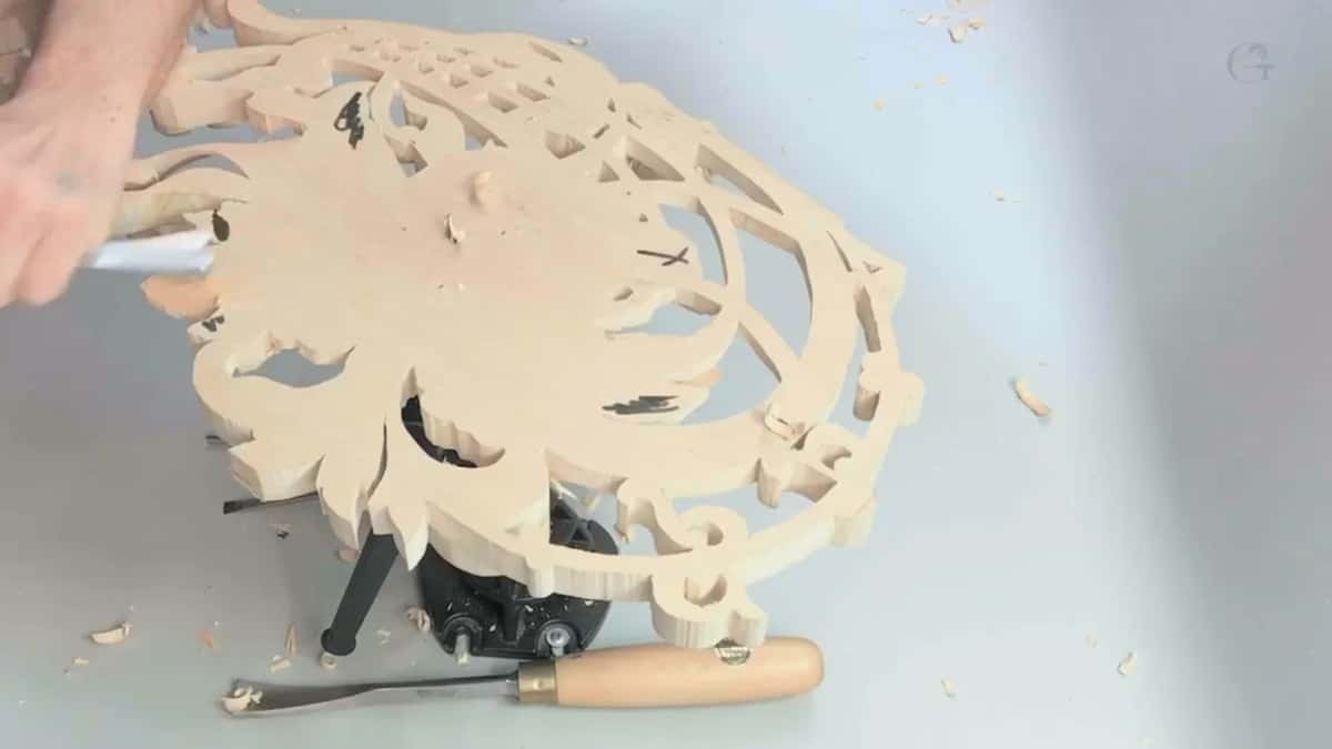Reverse side on the clamp, a hand at its left edge, a gouge on the bench below