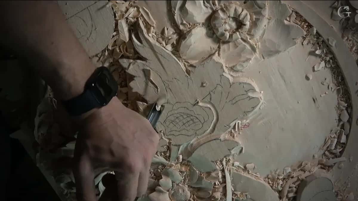 Hand low on the left side of the drawn flower, the blade down in the wood beneath it