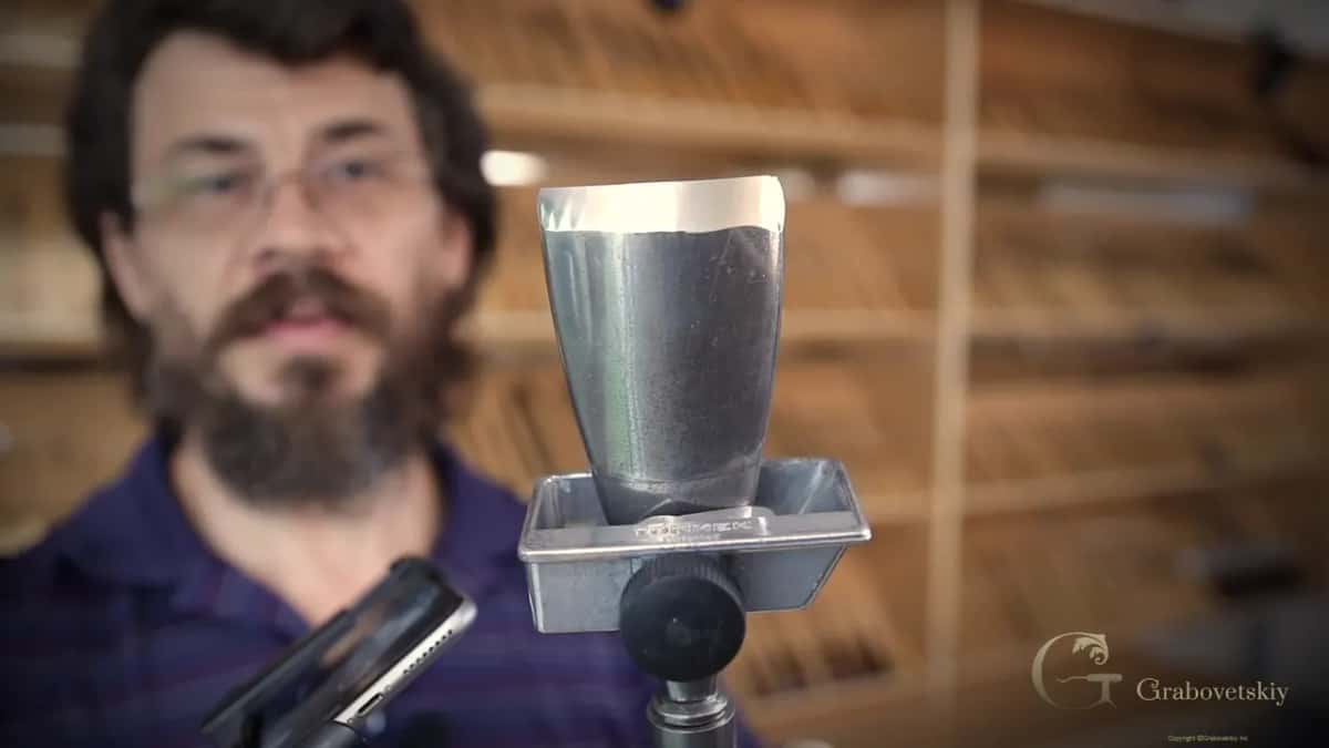 The finished bevel, mirror bright, clamped in a jig marked Tormek and held up to the camera against the tool wall.