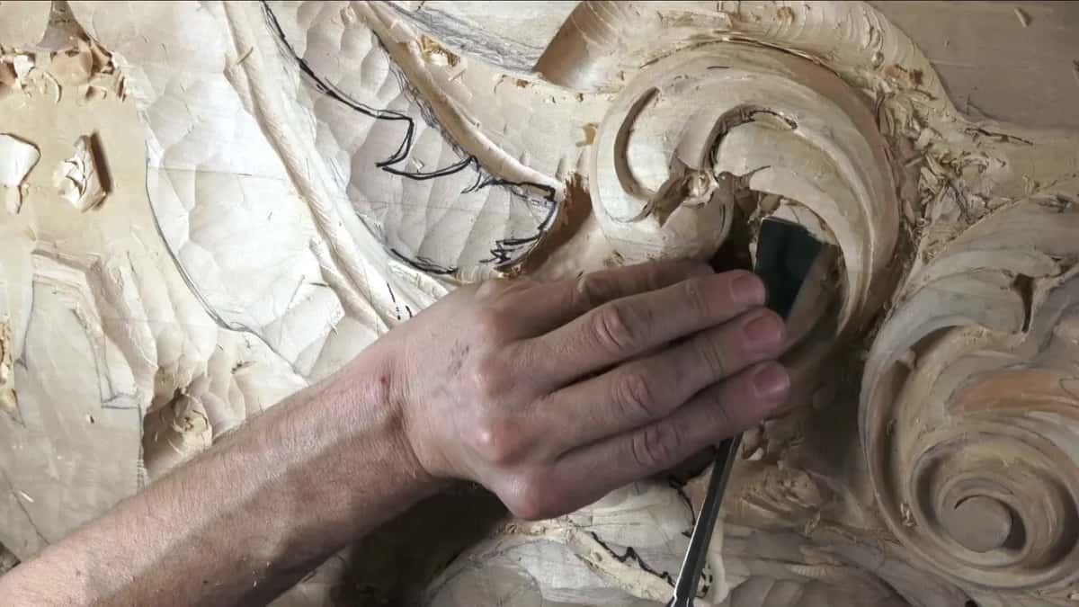 A flat blade running along the hollow under the curl, fingers at the bottom edge of the picture.