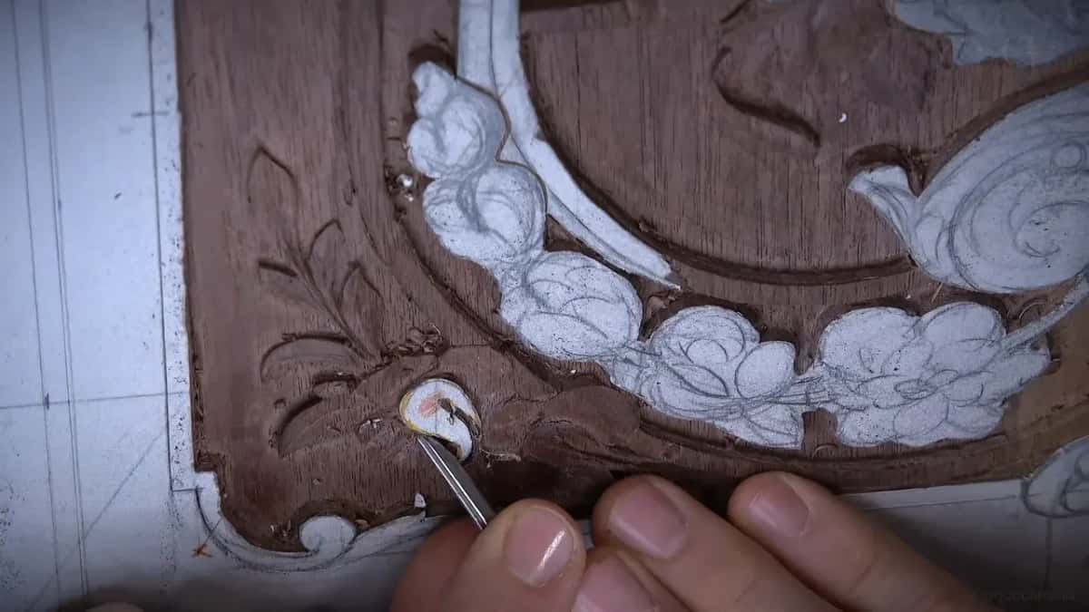 Blade point set into the marked flower, held between two fingers, with the carved corner running away behind it