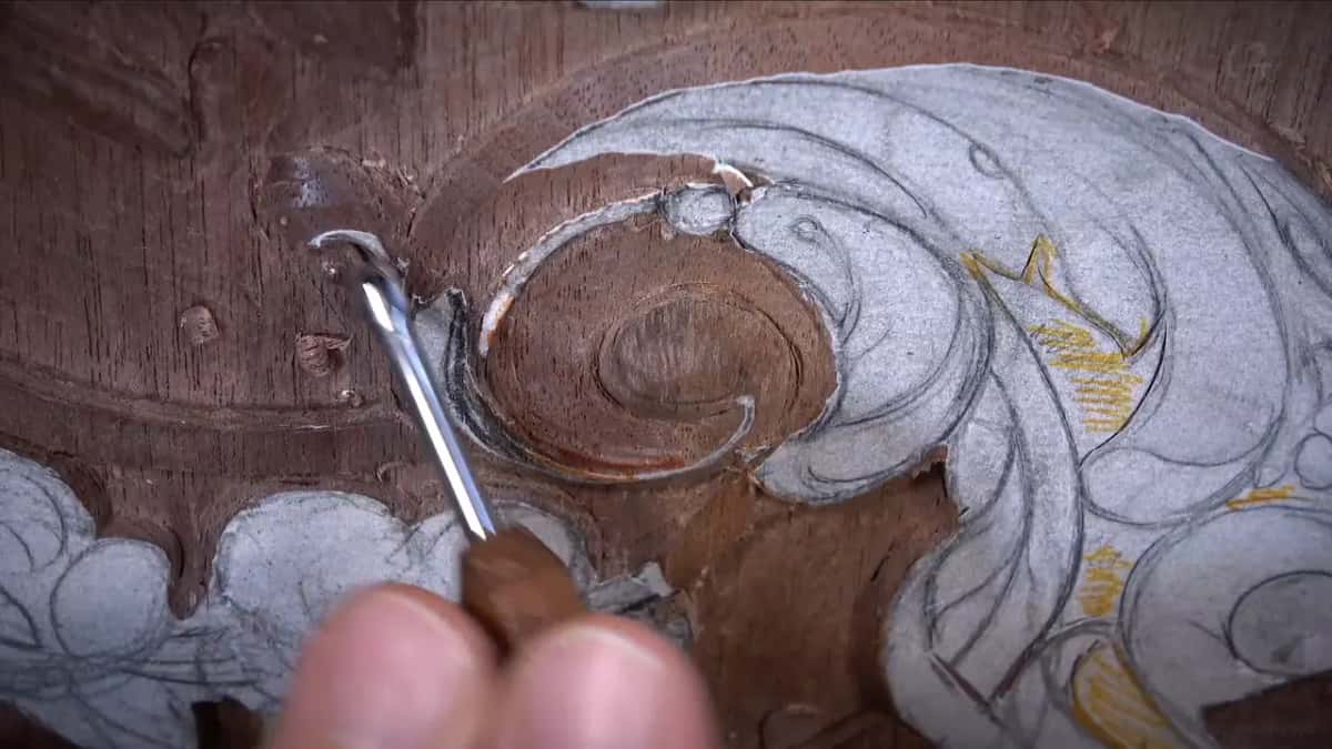 Veiner lifting waste out of the volute centre, the eye already cleared down to bare wood, yellow drawing above