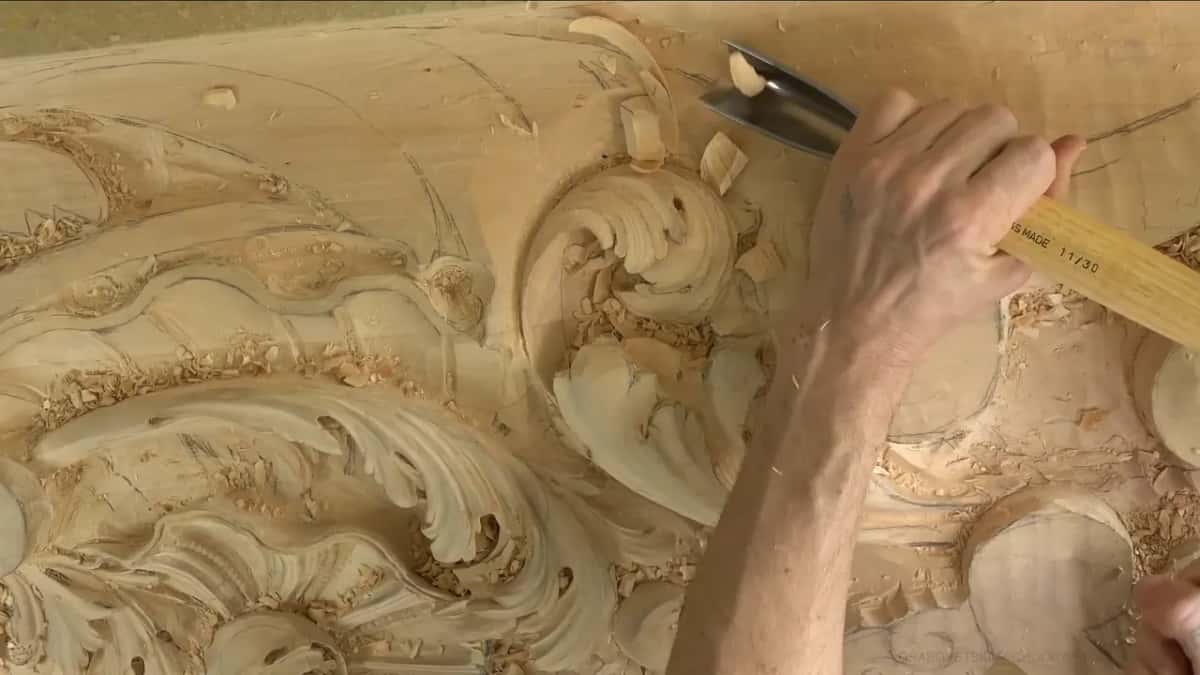 Seen from low down, the relief rises in scrolls as a hand brings a wide gouge in at the top.
