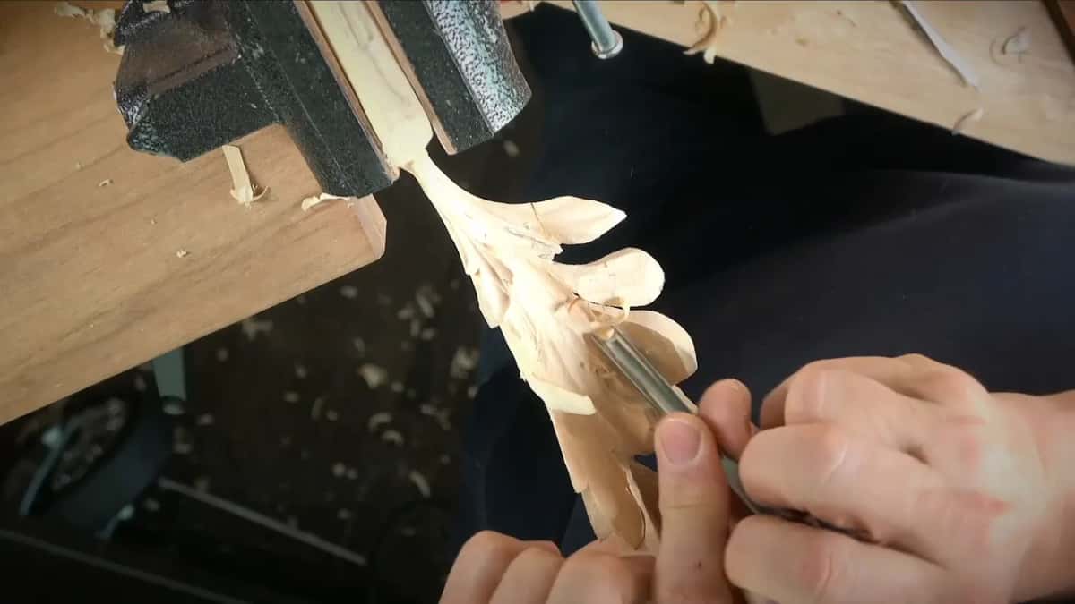 Leaf clamped in a small black vise while a gouge trims one edge from below
