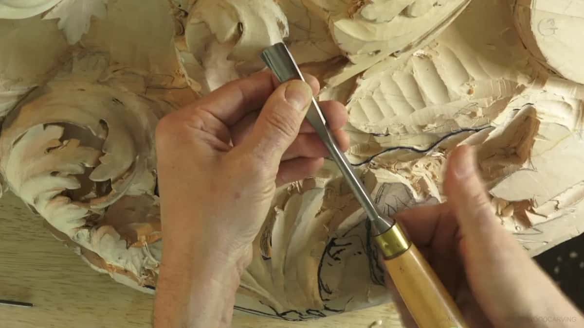 A gouge with a brass ferrule held up above the carving.