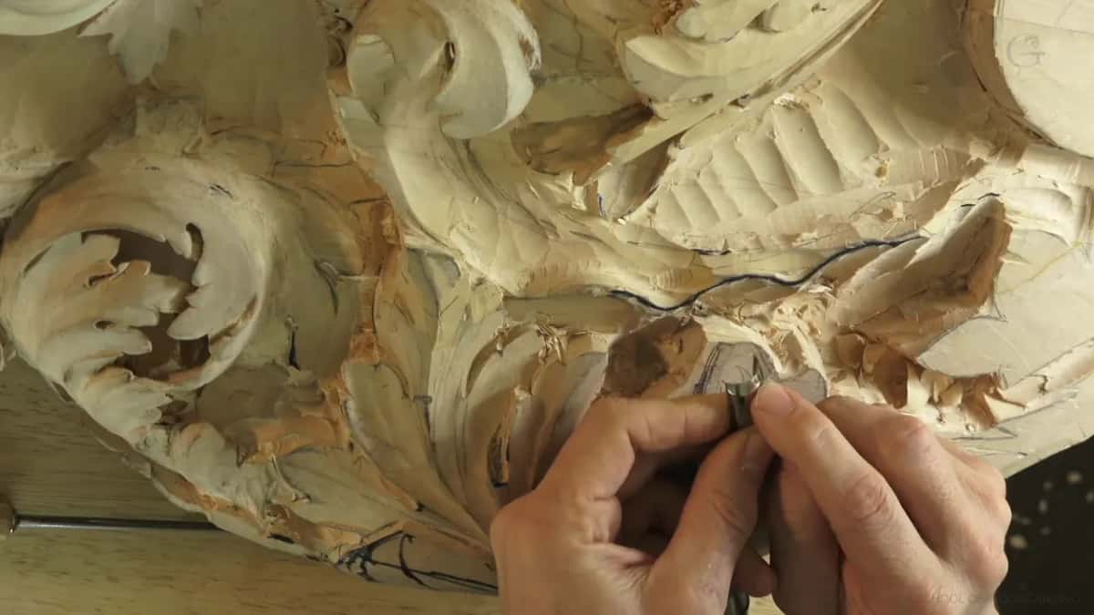 Both hands low on a small tool, the palm pressed flat against the wood.