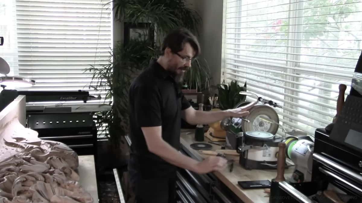 His hand rests on the Tormek wheel while spare discs lie on the bench beside it.