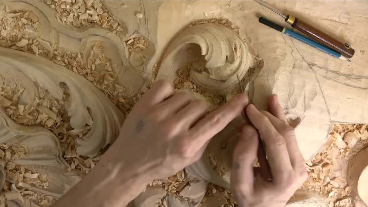Two hands steer a needle-thin tool into a small opening in the curl, a pencil above.
