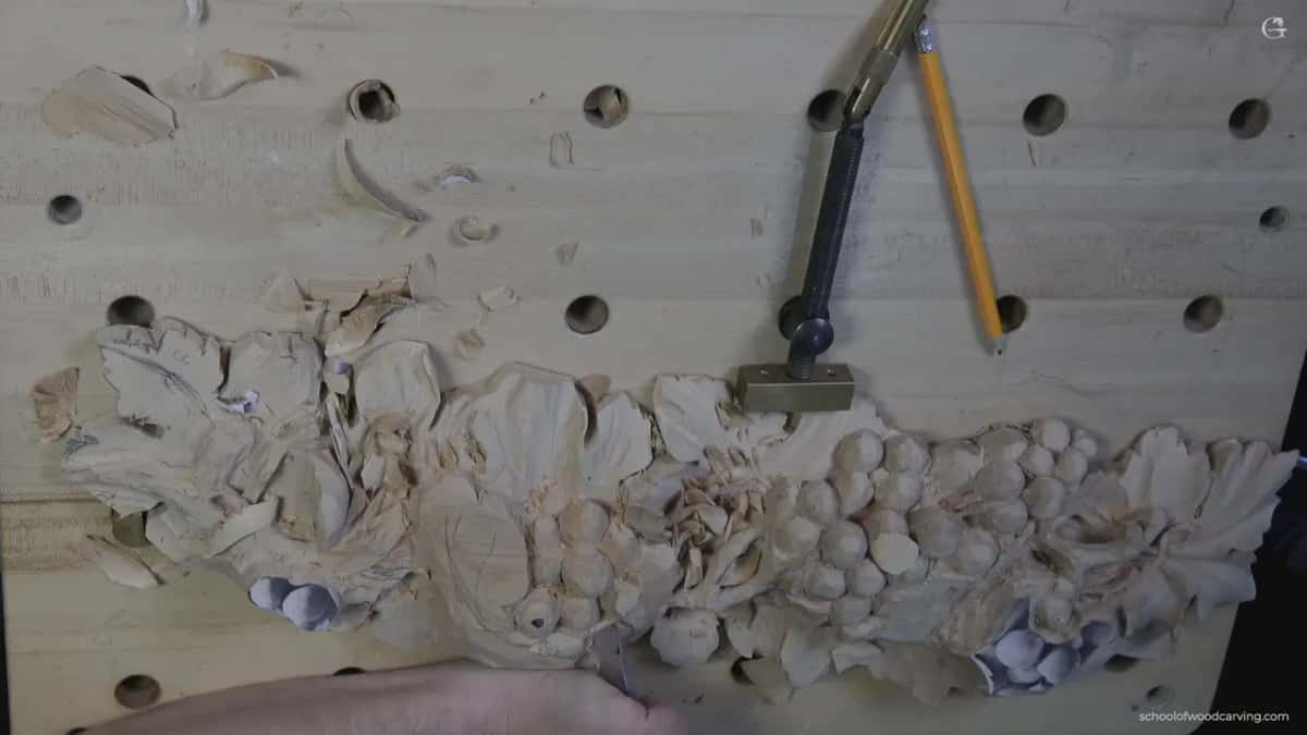Whole panel clamped to the bench, both grape clusters roughed in, a pencil and a gouge lying beside the work