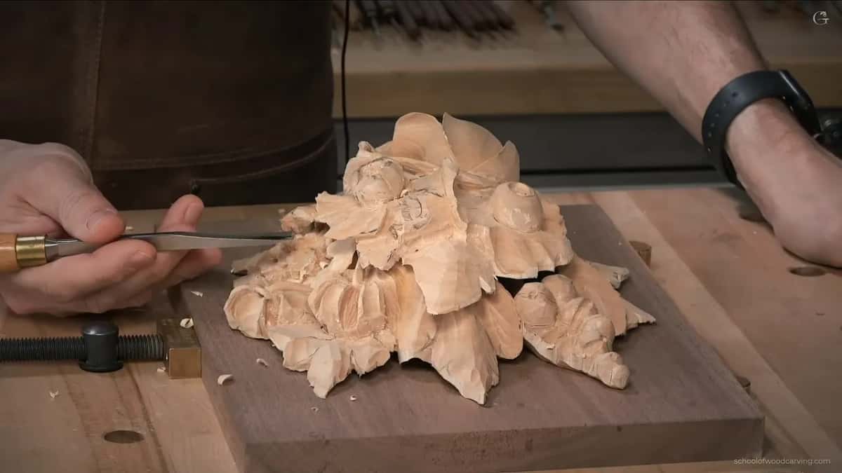 Low side view of the carving on its board, one hand on a brass ferruled tool