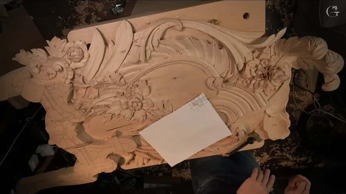The paper drawing lies flat on the carved panel while both hands wait below it