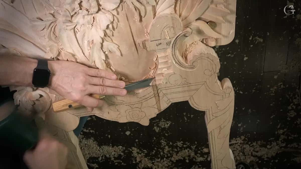 Left hand steadies a wide gouge held almost flat while the mallet waits at the edge