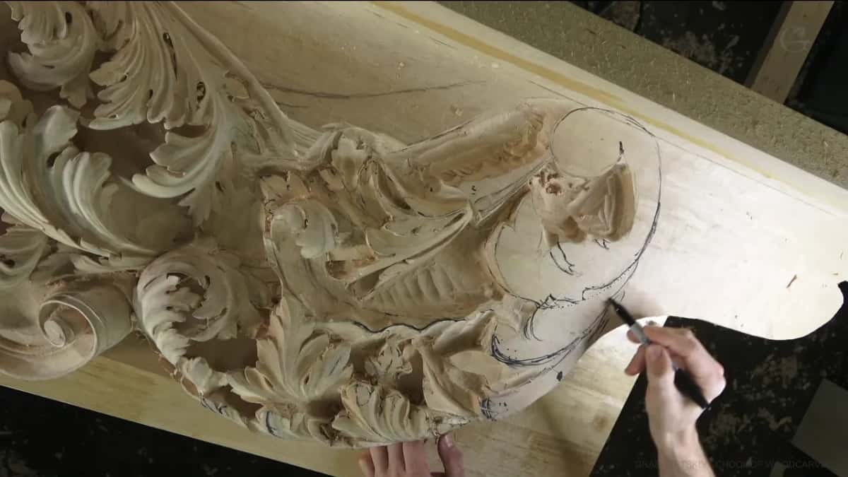 With a black marker in his right hand he adds lines to the flat corner, beside scrolls already carved.