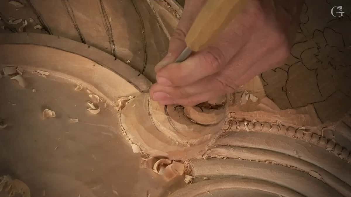 Close view of a gouge down in the scroll hollow, curls of wood beside it and flower drawings above