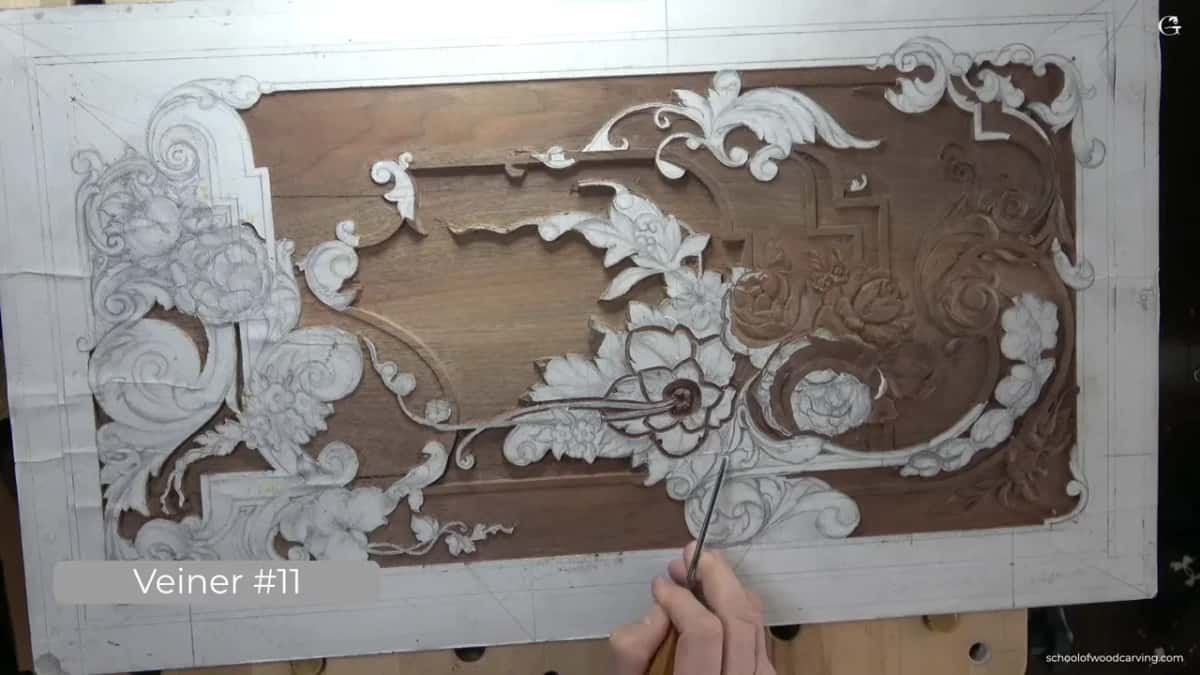 Seen from straight above, the ornament chalked white across dark walnut, with a veiner entering from the lower right corner.